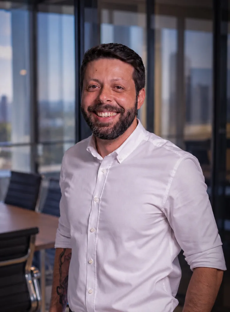 Marcelo Tebet, fundador da Vinq, sorrindo de camisa branca em uma sala de reuniões com vista para a cidade